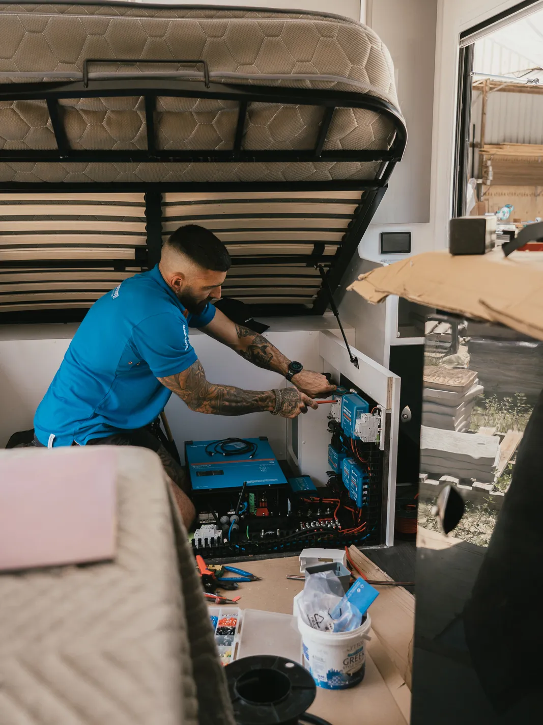 Jon installing a Victron lithium power system under the bed frame of a caravan